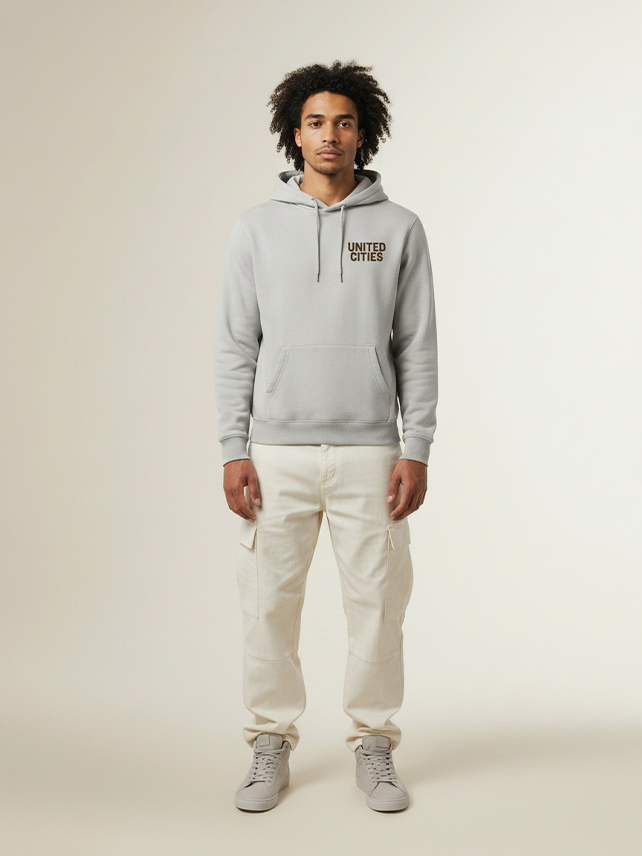 UNITED CITIES / ANTWERP Heavy Hoodie – Licht asfalt met donkerbruine, matte belettering. 65% katoen, 35% polyester, geborsteld fleece (300 g/m²). Ruime pasvorm.